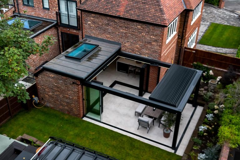 Aerial view of brick house extension with skylight, patio, outdoor pergola, dining set, and landscaped garden.