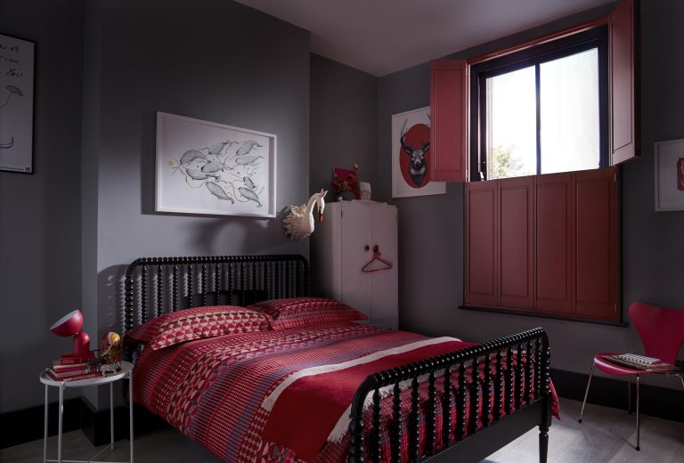 Bedroom with dark gray walls, black spindle bed frame, red patterned bedding, red shutters, and framed wall art.