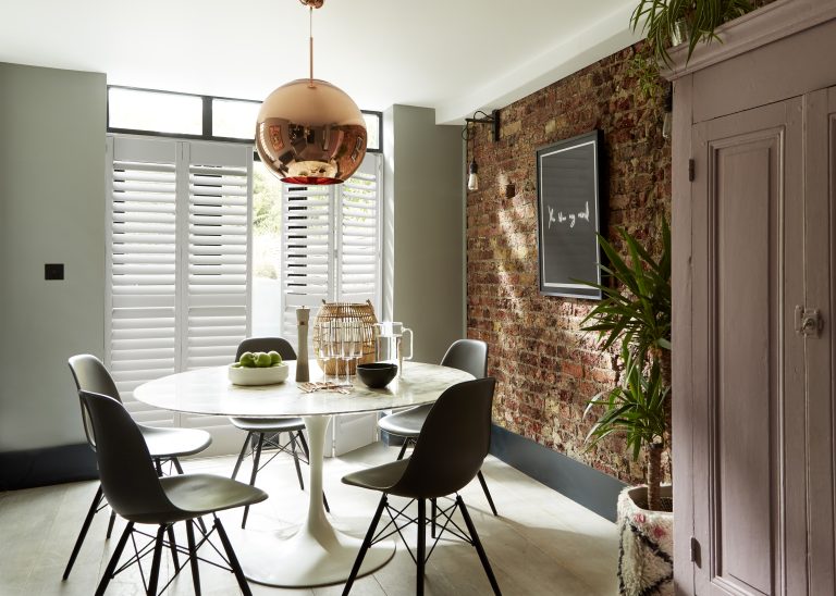 Modern dining room with marble tulip table, Eames chairs, copper pendant light, and exposed brick accent wall.