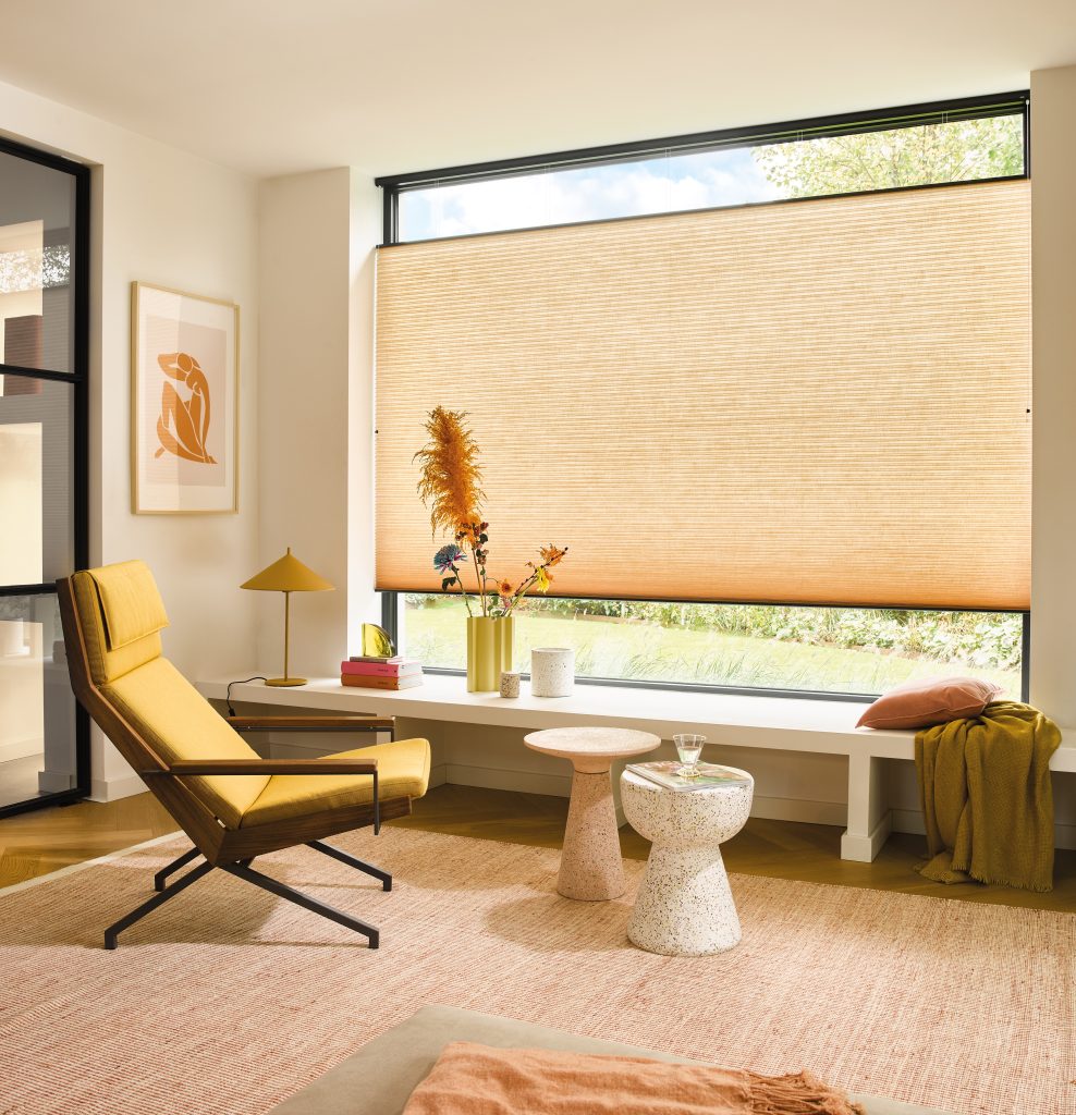 Modern living room with mustard yellow lounge chair, terrazzo side tables, and large window with textured roller blind.