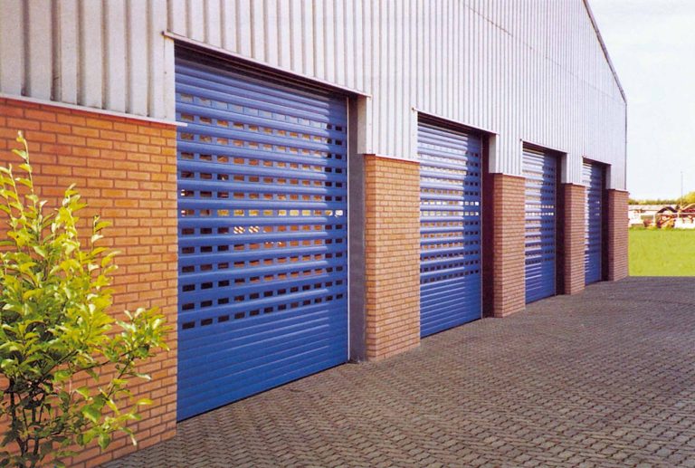 Industrial warehouse with brick walls and multiple blue perforated roller shutter doors along the exterior facade.