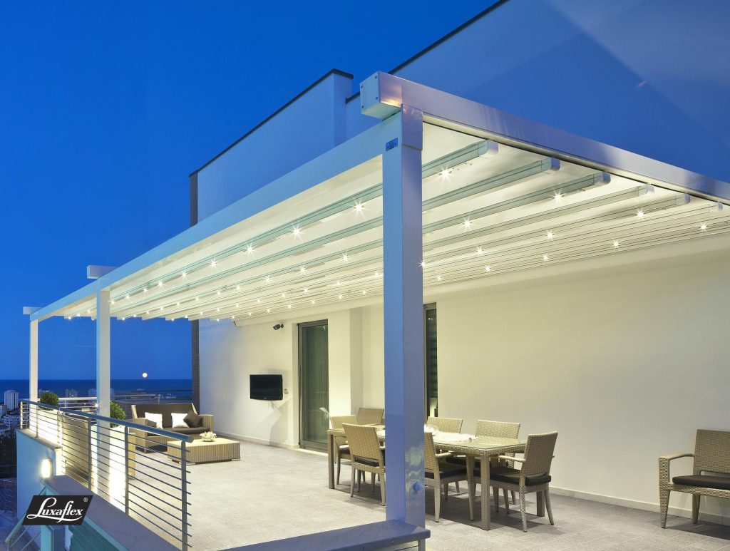 Luxaflex retractable roof pergola with LED lighting over rooftop terrace, ocean view at twilight, modern outdoor living space