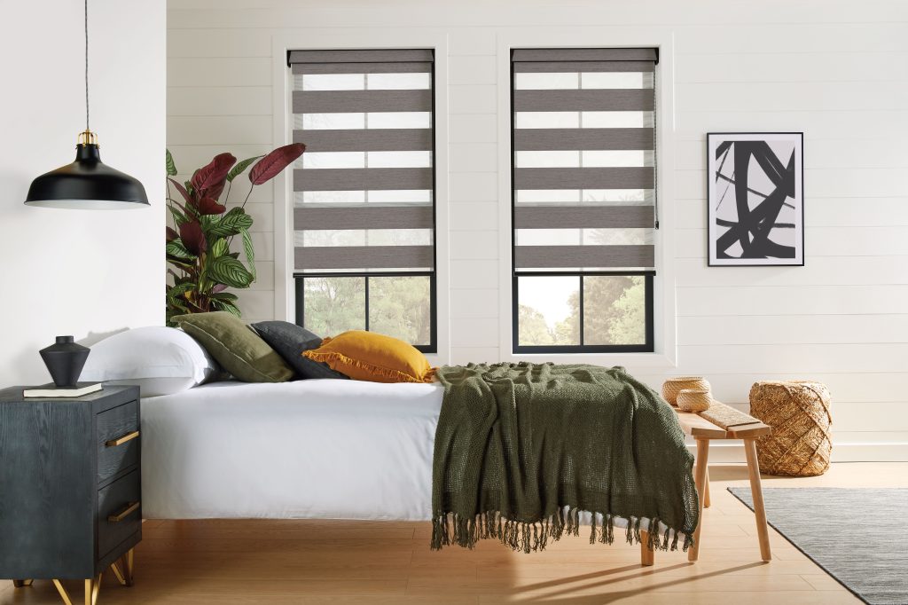 Modern bedroom with zebra shade windows, white bed, olive throw, mustard pillow, black nightstand, and abstract wall art.