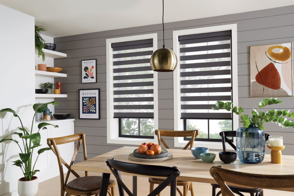 Modern dining room with gray shiplap wall, zebra blinds, brass pendant light, wooden table, and Matisse art prints.