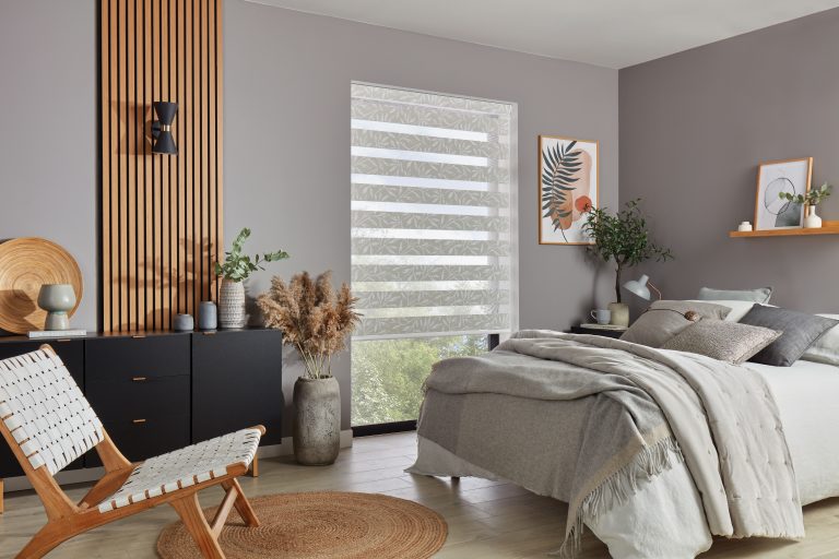 Modern bedroom with wood slat accent wall, black dresser, layered blinds, wall art, and gray bedding with pampas grass decor.