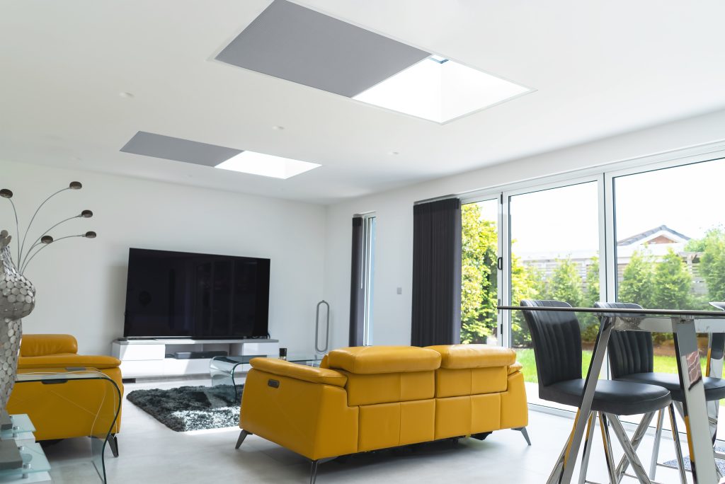 Modern living room with mustard leather sofas, skylights, large glass doors, and garden view