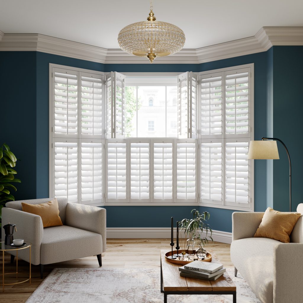 White plantation shutters on bay window in blue living room with gold chandelier and cream armchairs