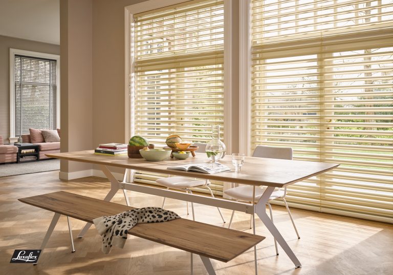 Bright dining room with cream Luxaflex venetian blinds, wooden table, bench, and fresh fruit bowls on herringbone floor.