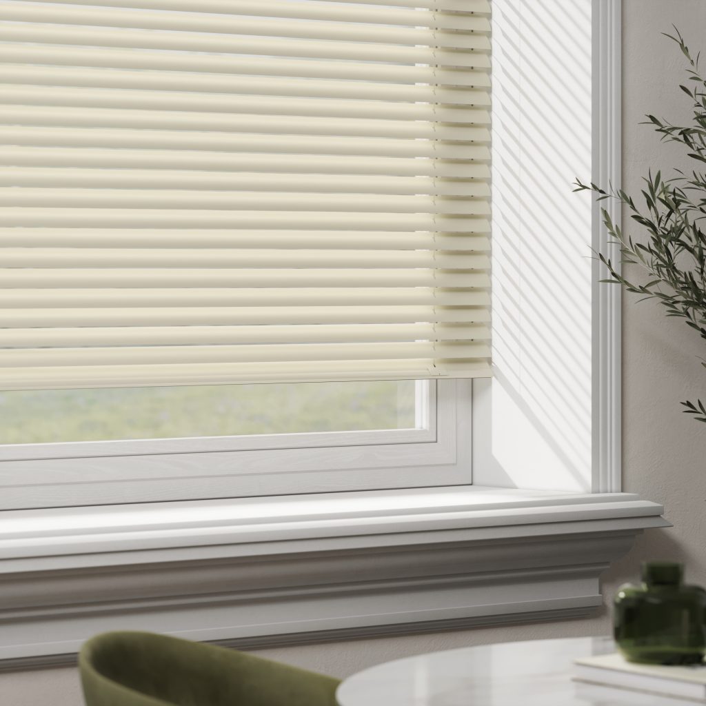 Cream venetian blinds partially covering a bright window with white sill, olive branch, and green chair in modern interior