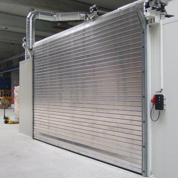 Industrial roller shutter door with metal slats in a warehouse, control panel mounted on side wall.