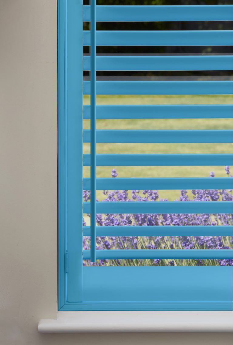 Turquoise plantation shutters on window overlooking lavender field and green lawn on sunny day